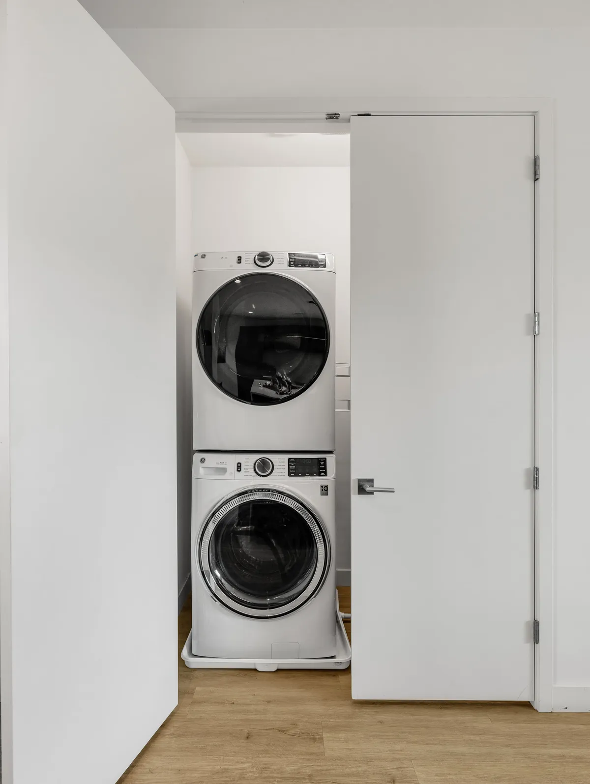 A compact, organized laundry space with a stacked washer and dryer unit, white doors, and wood flooring. The area feels functional and efficiently designed, highlighting utility.