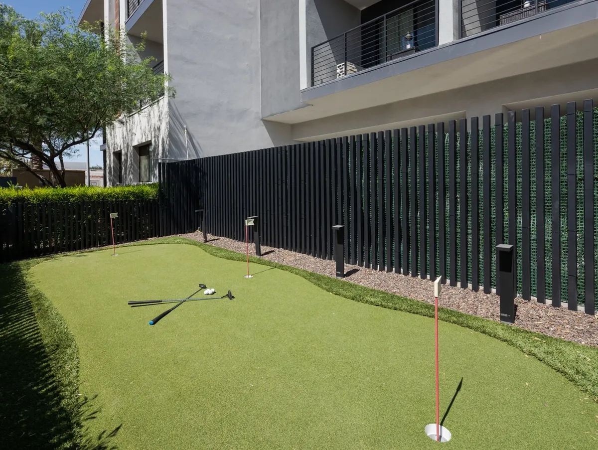 A modern, well-landscaped putting green complete with golf clubs, surrounded by manicured greenery and contemporary architecture. The area invites residents to practice their golf skills or simply relax in a sunny, scenic setting.