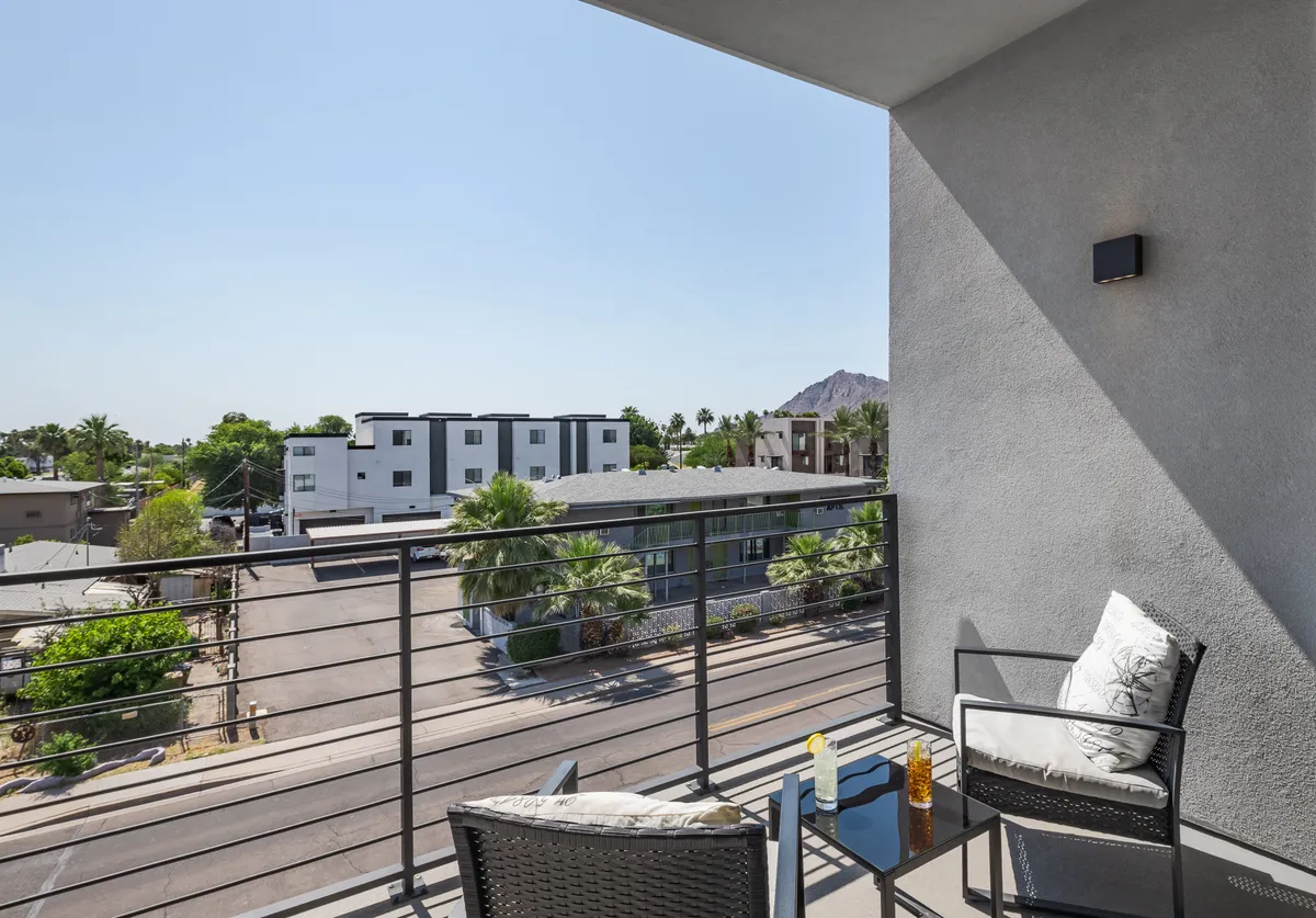 A private balcony furnished with cozy seating, offering a view over the street with a mountain backdrop. The scene captures a tranquil moment ideal for enjoying morning coffee, relaxing in the evening, or sharing conversation as the sun sets.