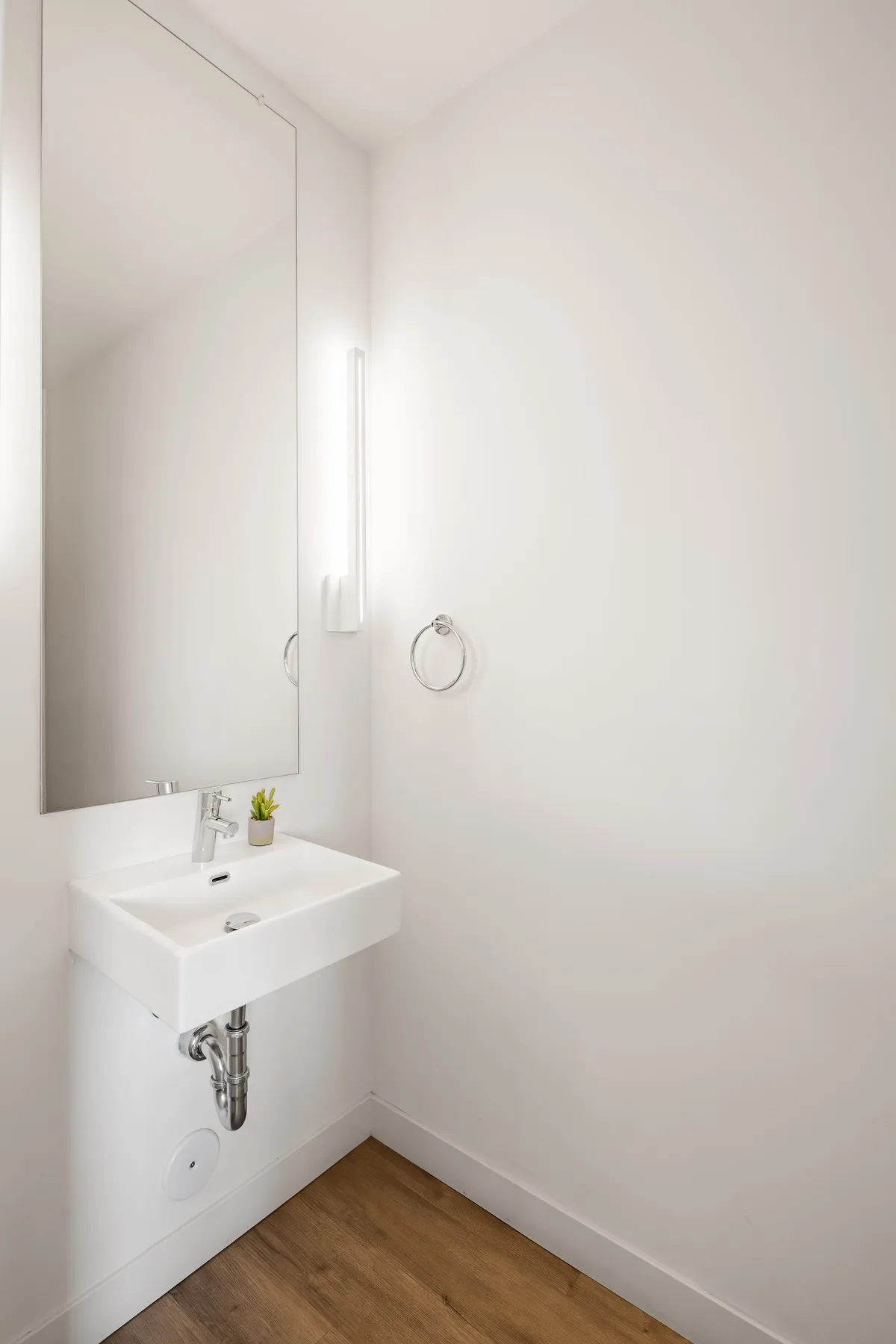 A serene and tidy bathroom featuring a modern sink, round mirror, and a small potted plant. The setting is minimal yet inviting, with calming tones that reflect cleanliness and care.