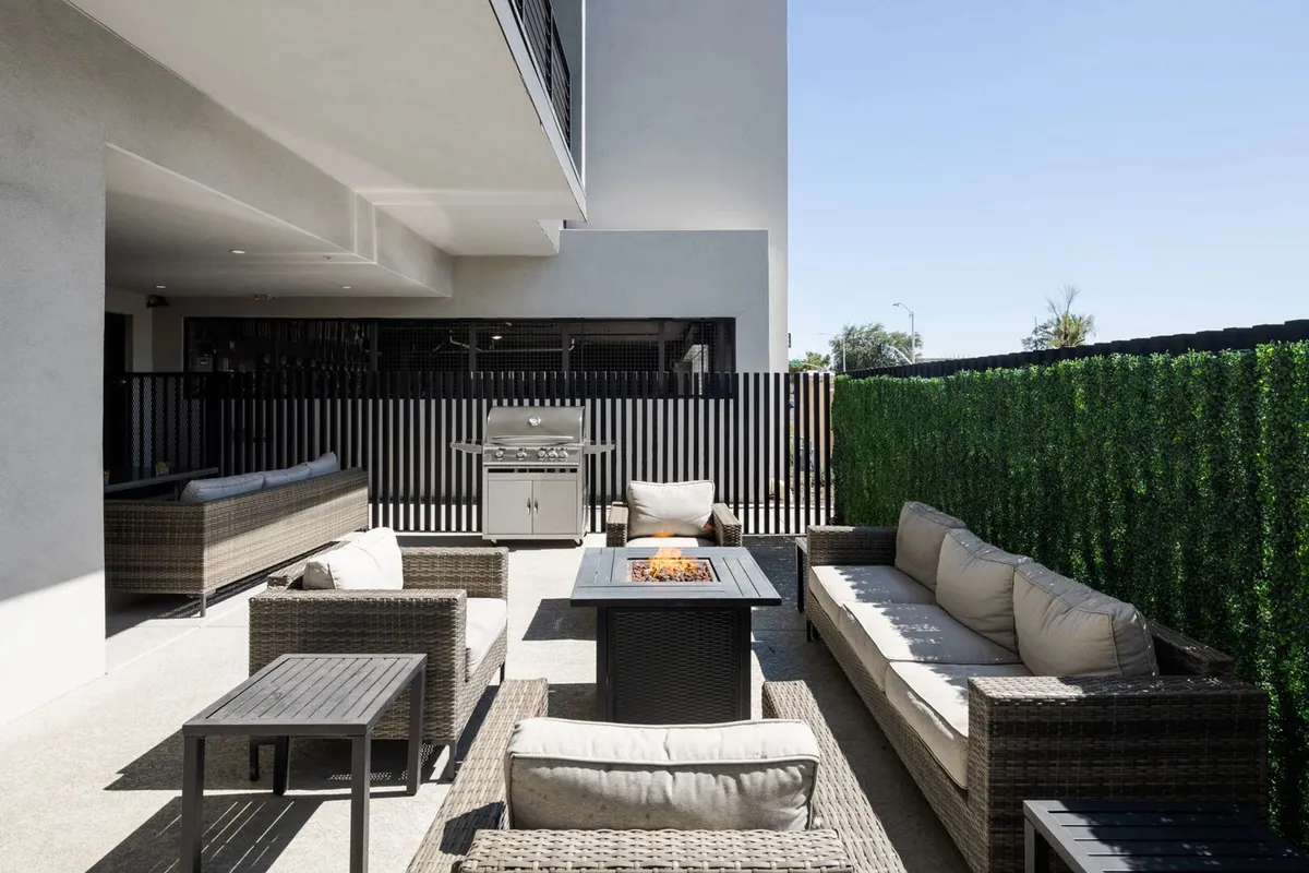 A welcoming exterior space centered on a fire pit, surrounded by comfortable outdoor seating and a BBQ grill. The greenery and open-air design create an inviting setting for socializing, dining, and enjoying evenings under the stars.