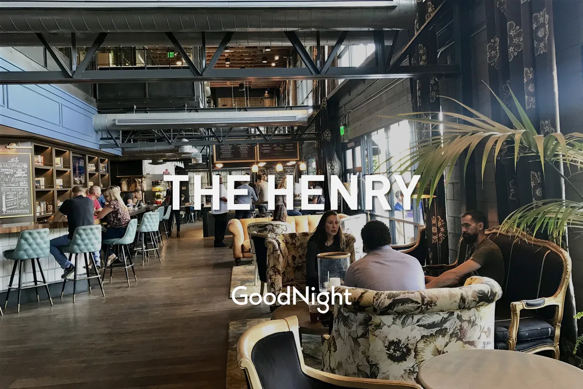 A stylish and lively interior bar scene with people gathered around a modern bar, floral chairs, and groups socializing. The setting is warm and welcoming, filled with animated conversations and signature drinks.