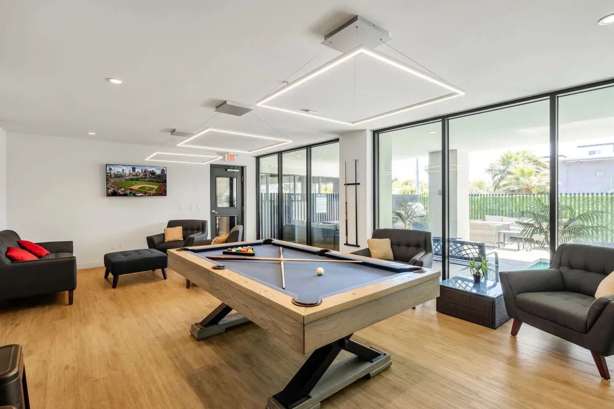 This image shows a stylish interior community clubhouse featuring a pool table, comfortable sofas, a television, and large windows that flood the space with natural light. The open layout encourages mingling and social activities, embodying the feel of a high-end, resort-style amenity space.